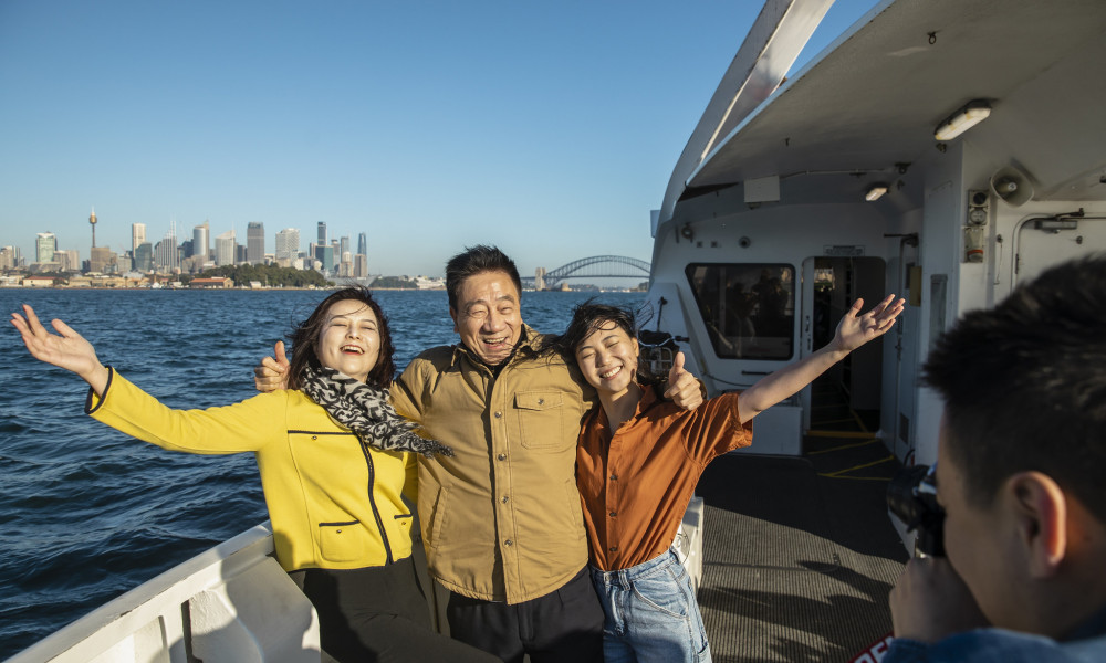 3 students on a boat posting for a photo with Sydney City in the distance